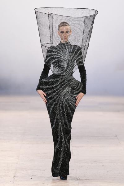 这组细节图展示的是 拉胡尔·米什拉Rahul Mishra 2026 春夏高级定制系列。旋涡结构、火焰廓形、水流纹样与巨大环形头饰构成超现实视觉体系，秀场更像一场关于宇宙元素的艺术实验。黑色系列表现引力与深空，银白色象征流体能量，而火焰红与熔岩橙则演绎自然再生。设计师继续以印度手工刺绣技术承载未来主义语言，将高定推进至雕塑与装置艺术边界。——来自顽石频道国际流行趋势分析。